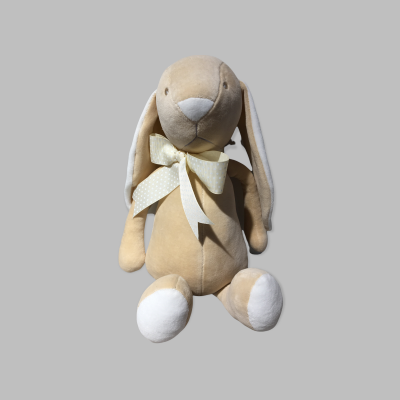 Coelho de peluche bege com fita amarela com bolinhas brancas sentado