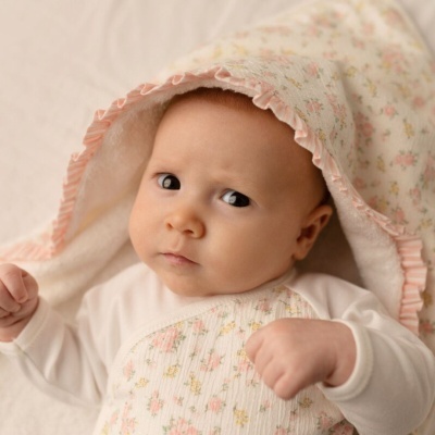 Bebé com cobertor floral e roupa branca rosa