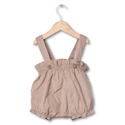 Jardineira de bebé bege em tecido com alças largas pendurada num cabide de madeira