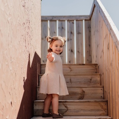 Menina pequena com vestido rosa claro e sapatos castanhos numa escada de madeira
