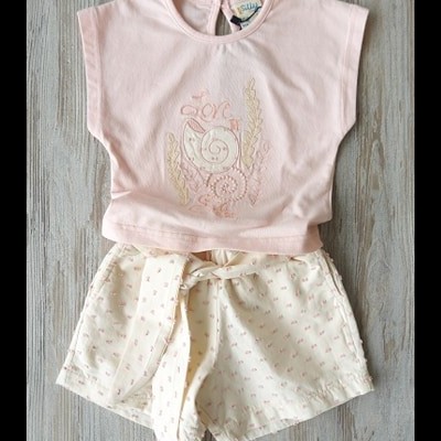 Conjunto de t-shirt rosa e calções brancos com padrão cor-de-rosa sobre madeira cinza.