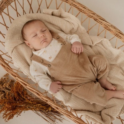 Bebé a dormir numa cesta de vime com roupas bege e branca