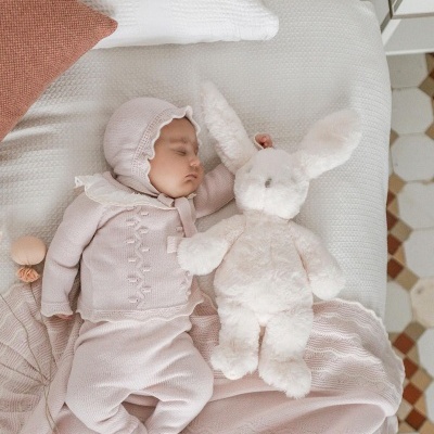 Bebé a dormir com conjunto de malha cor-de-rosa e peluche de coelho branco na cama