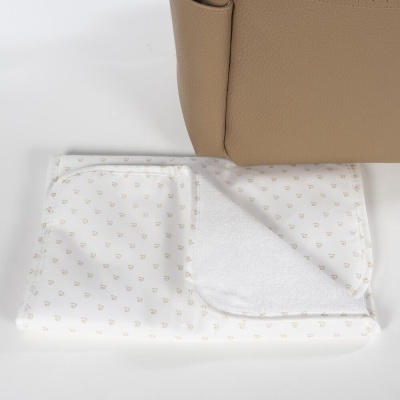 Toalhinha branca com padrões dourados junto a uma bolsa bege