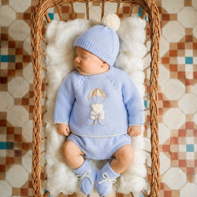 Bebé a dormir em cama de vime com roupa azul de malha