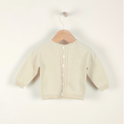 Casaco de malha bege para bebé num cabide de madeira