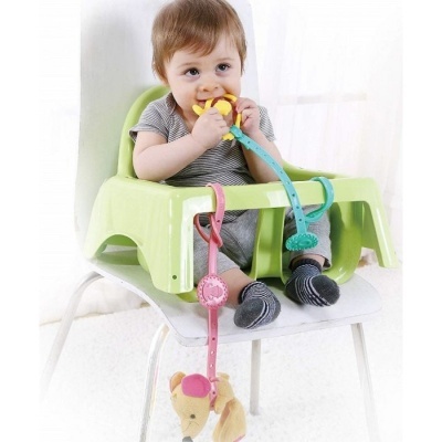 Bebé sentado num assento verde claro com brinquedos pendurados em cordões azuis e rosa.