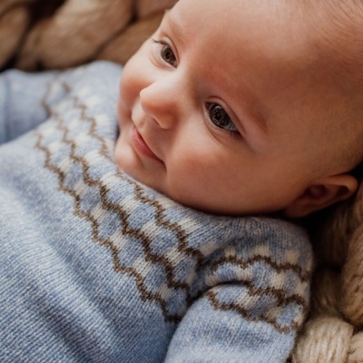 Bebé de pele clara deitado com camisola de malha azul com padrão de zigzag.