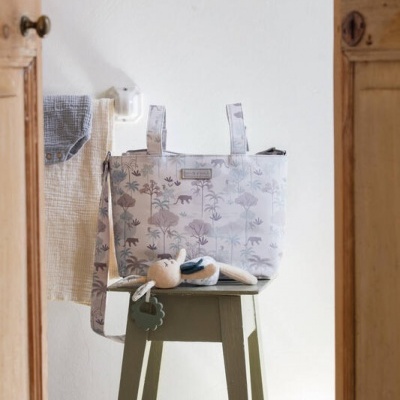 Bolsa de maternidade com padrão de árvores e animais sobre banco verde e toalhas penduradas