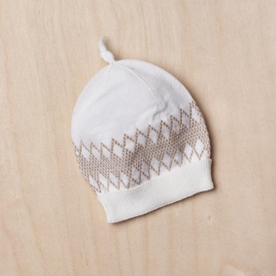 Gorro de malha branco com padrão geométrico castanho sobre fundo de madeira clara.