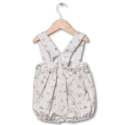 Macacão curto bege claro para bebé com alças e padrão colorido, pendurado num cabide de madeira.
