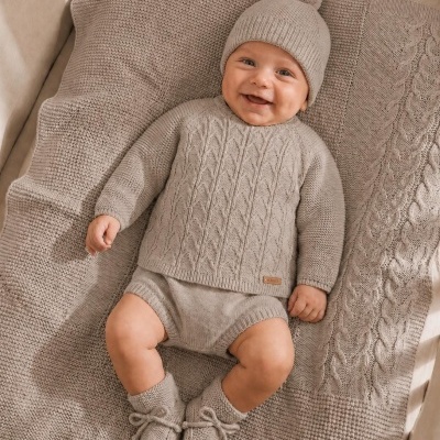 Bebé sorridente vestido com conjunto bege de malha, deitado em manta bege de malha