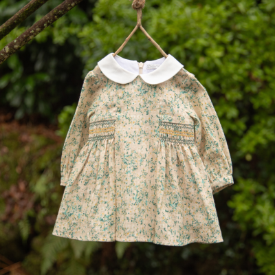 Vestido infantil creme com estampa floral verde e gola branca pendurado ao ar livre