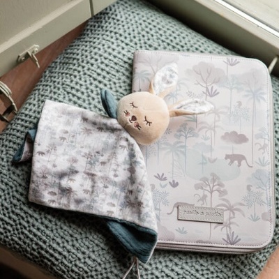 Cobertor de bebé com cabeça de coelho e estojo com padrão natural sobre manta cinzenta junto a janela.