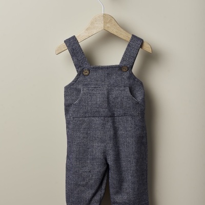 Jardineira infantil cinza escuro com botões de madeira num cabide.