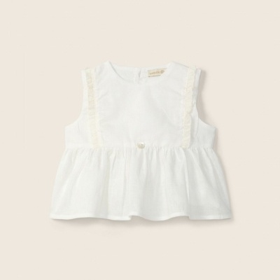 Blusa branca para criança com renda e botão pequeno sobre fundo bege