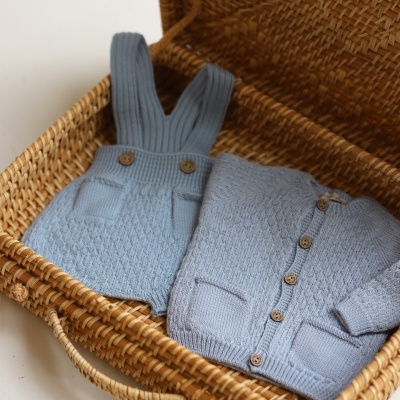 Conjunto de roupa de bebé azul claro em malha numa cesta de verga.
