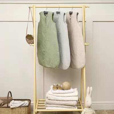 Sacos de dormir para bebé pendurados num cabide de madeira clara com brinquedo coelho ao lado