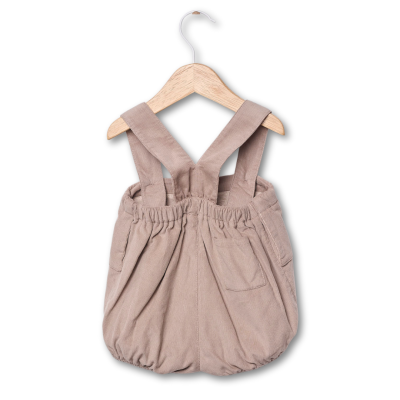 Macacão infantil bege de veludo cotelê com alças cruzadas pendurado em cabide de madeira