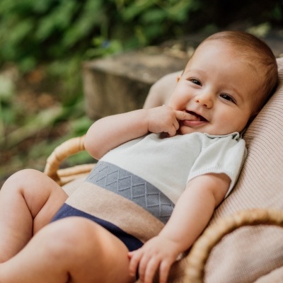 Bebé numa cadeira de vime com roupa de malha azul, bege e cinza