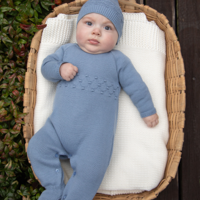 Bebé de fato azul de malha numa cesta de vime com manta branca