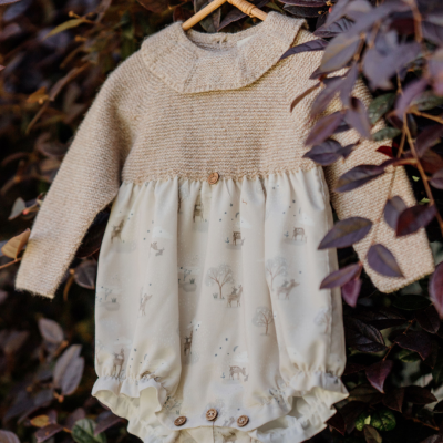 Macacão de bebé bege e branco com padrão de animais, pendurado em cabides