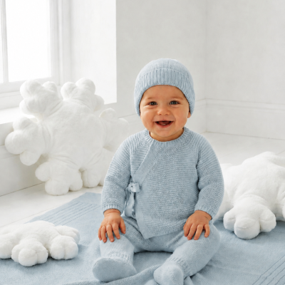 Bebé com roupa de malha azul claro sentado em tapete azul com almofadas brancas em forma de flocos de neve