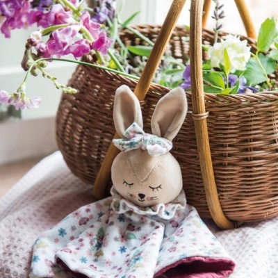 Urso de peluche com roupa floral junto a cesto de vime com flores