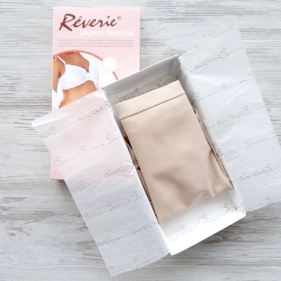 Caixa de lingerie maternal Réverie com sutiã bege dentro e embalagem rosa ao fundo