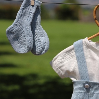 Meias e roupa de bebé em malha azul clara e branca penduradas ao ar livre