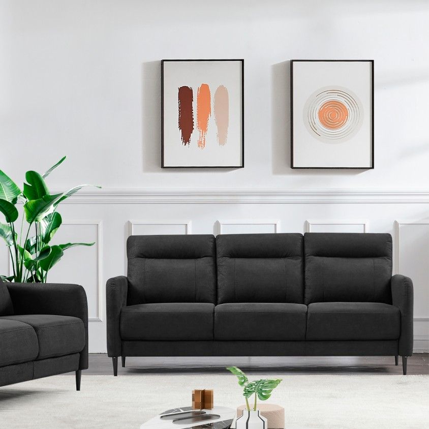 sofá cinzento escuro de três lugares numa sala com paredes brancas, duas pinturas e planta