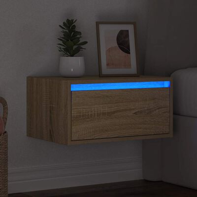 Mesa de cabeceira suspensa em madeira clara com luz azul e decoração com planta e quadro.