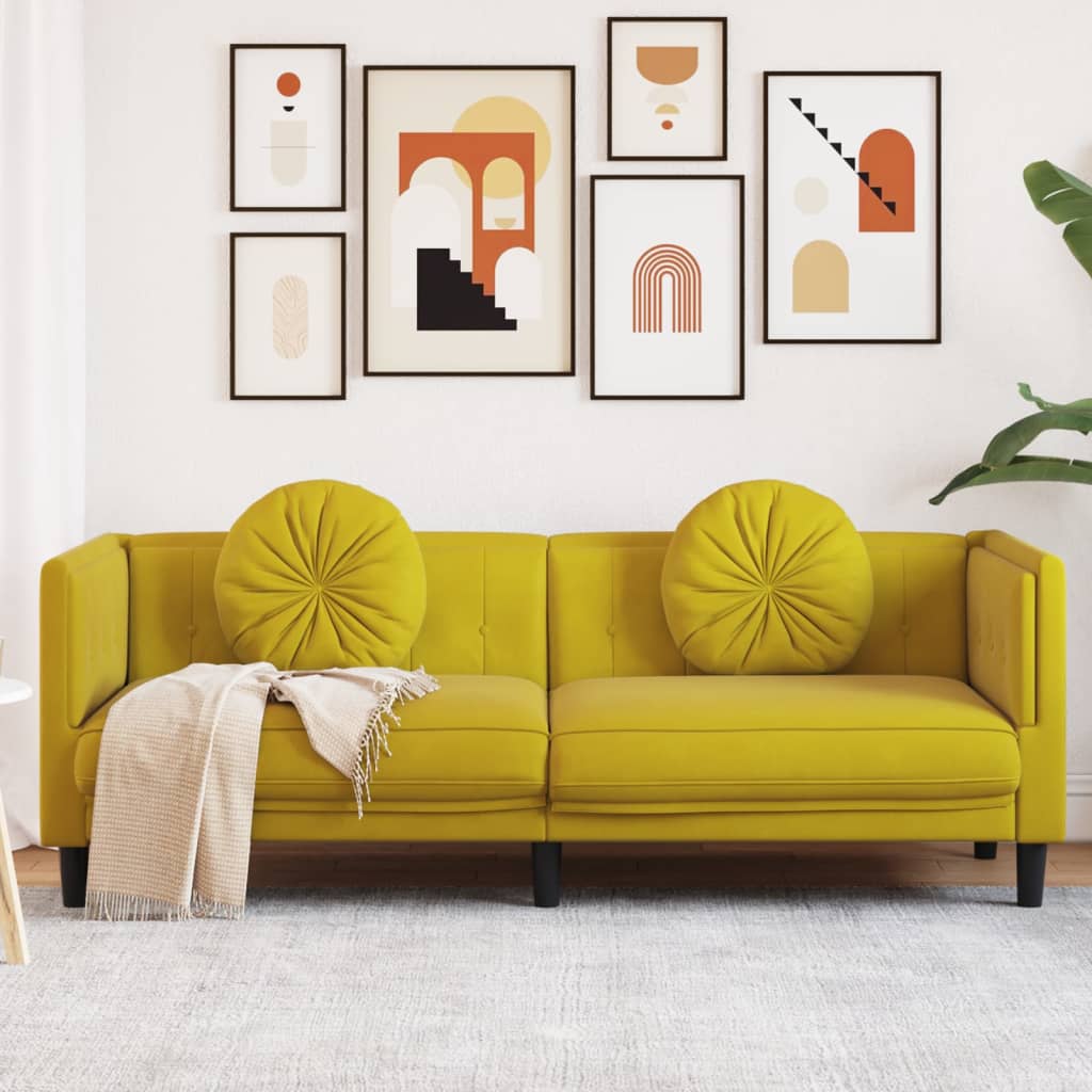Sofá amarelo com almofadas redondas e manta bege numa sala com quadros geométricos na parede.