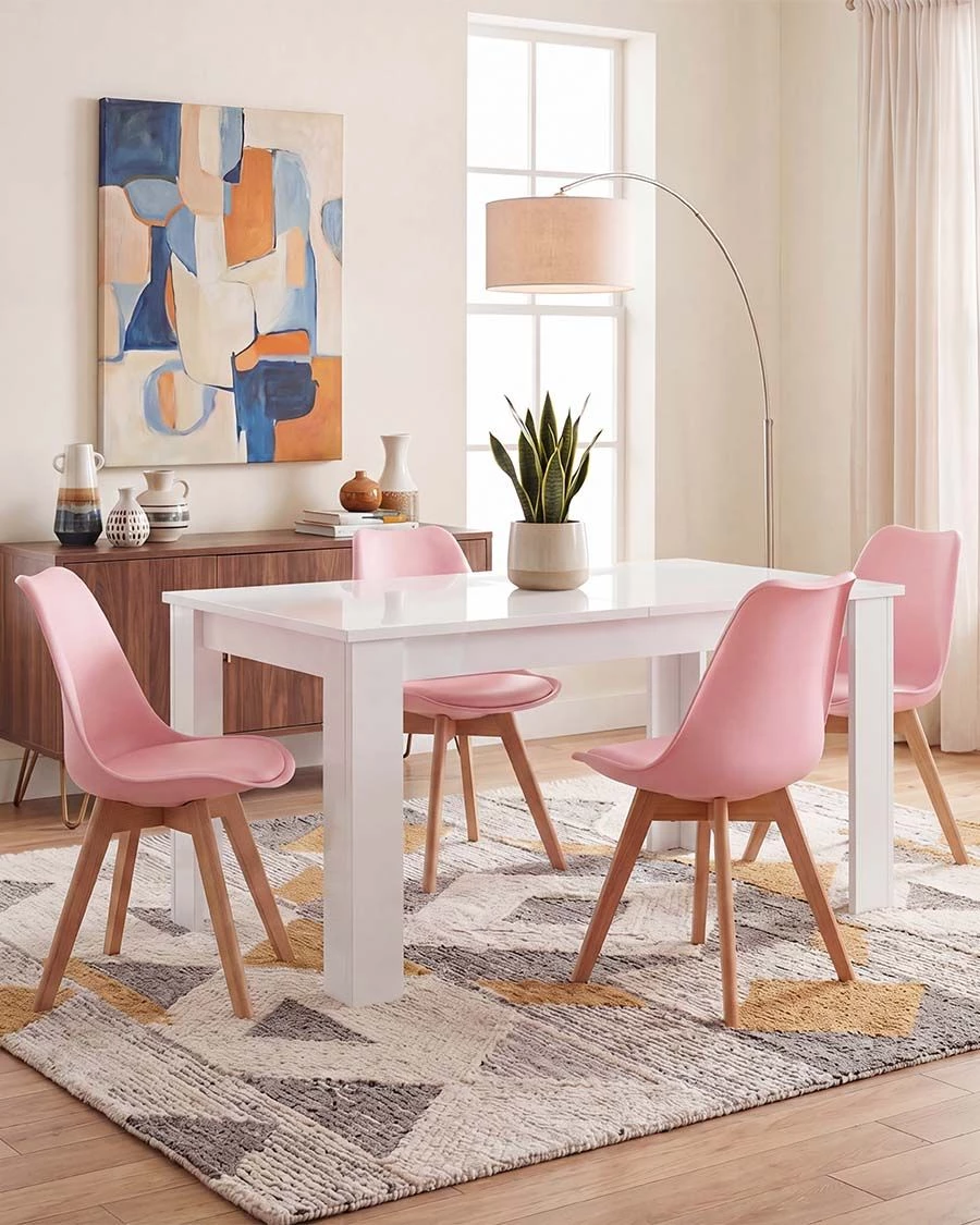 Conjunto de mesa branca com quatro cadeiras cor-de-rosa numa sala de jantar iluminada e decorada com móvel, quadro, planta e candeeiro