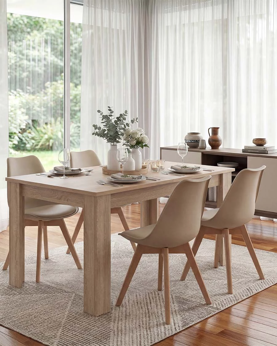Mesa de jantar em madeira clara com cadeiras bege e decoração com flores em sala iluminada