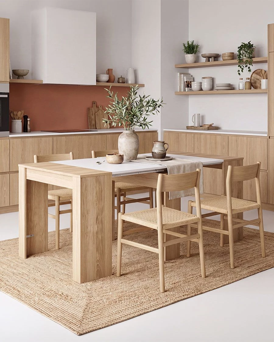 Mesa de jantar extensível de madeira clara com cadeiras de madeira e assentos em fibra natural num ambiente de cozinha moderna.