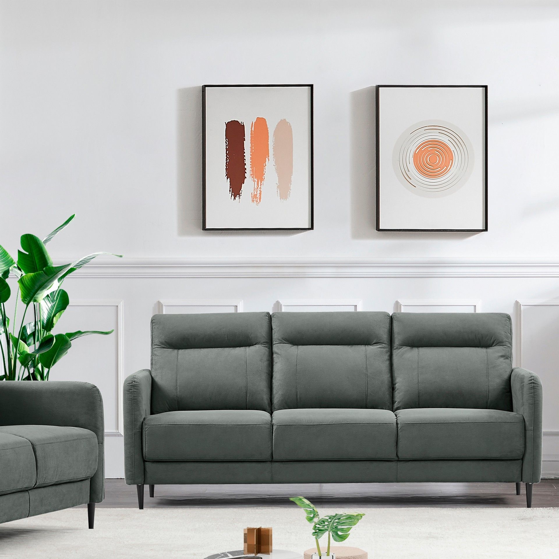 Sofá cinzento escuro de três lugares numa sala com paredes brancas e duas pinturas abstratas.