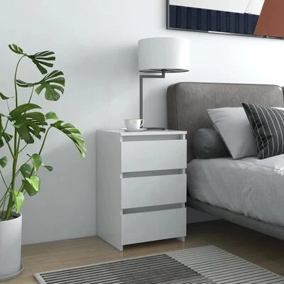 Móvel branco com três gavetas, candeeiro e chávena, cama cinza com almofadas, planta e tapete