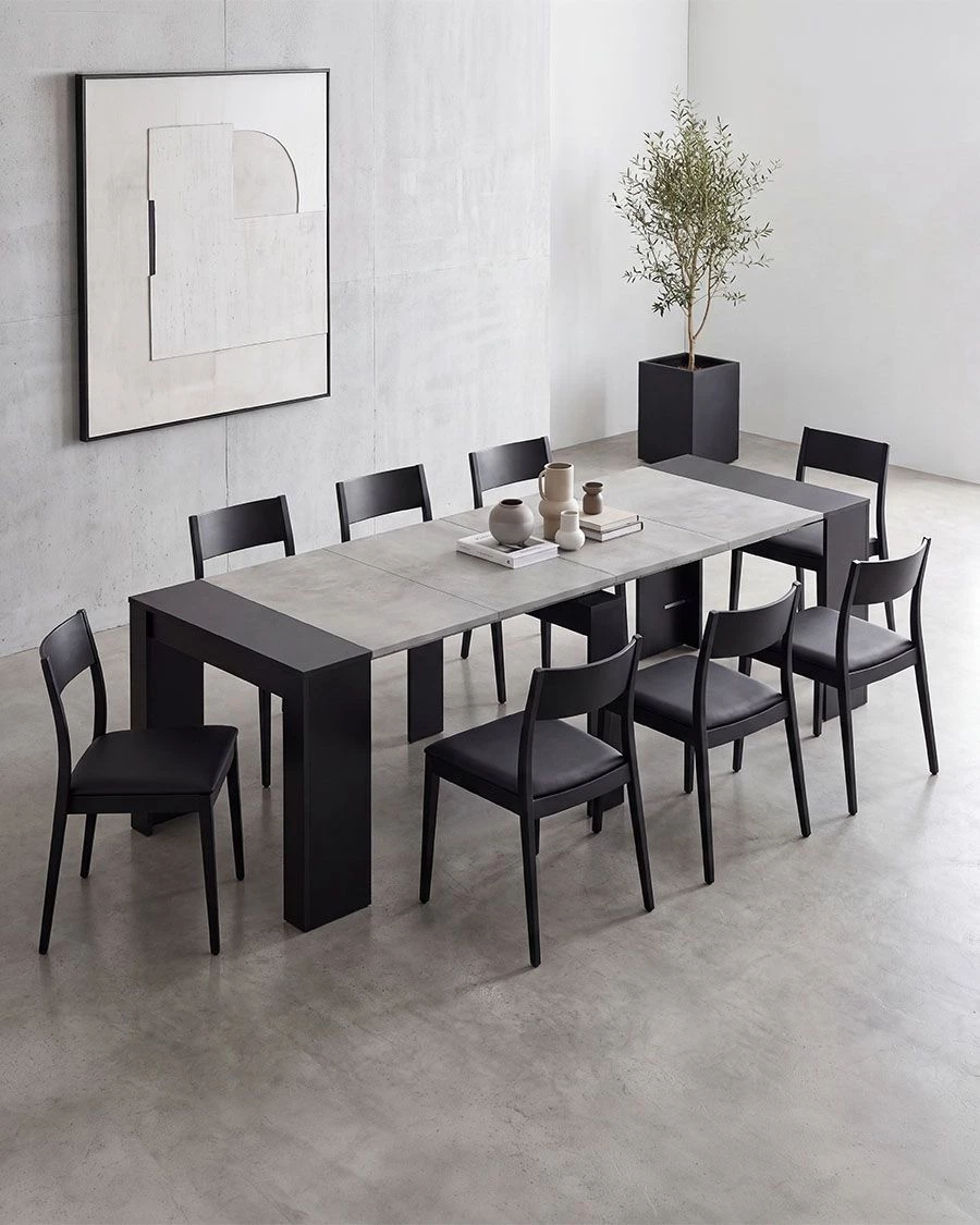 Mesa de jantar cinza com cadeiras pretas e vasos decorativos num ambiente minimalista