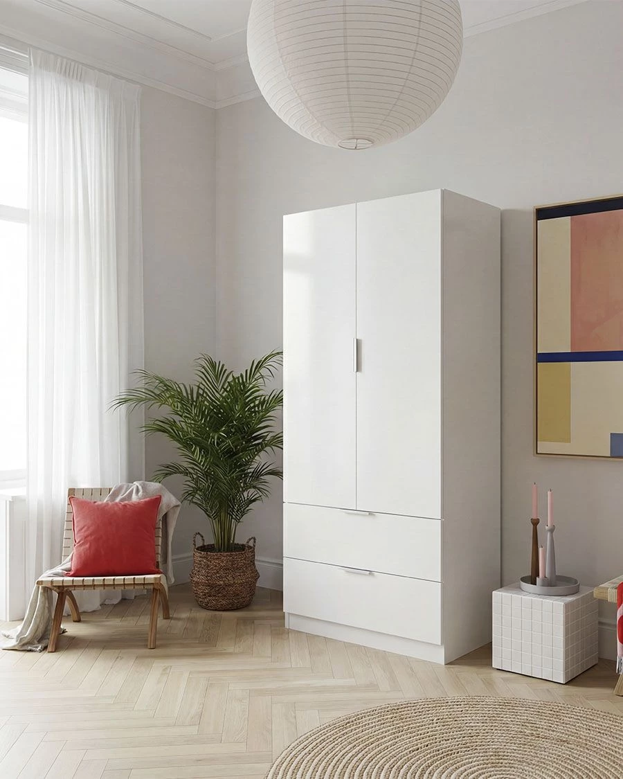 Armário branco de madeira com duas portas e gavetas numa sala, cadeira com almofada vermelha e planta em vaso ao lado