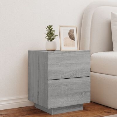 Mesa de cabeceira cinzenta com duas gavetas junto a cama bege e vaso com planta