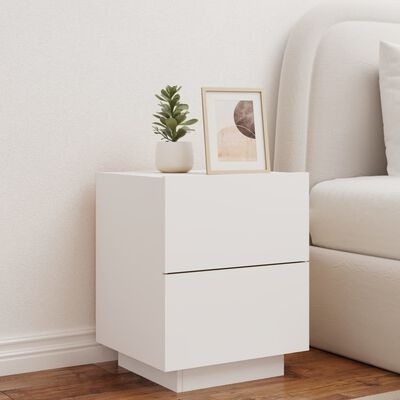 Móvel de apoio branco com duas gavetas junto a cama, com planta e moldura decorativa