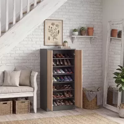Armário sapateira com portas castanho claro e estrutura cinza escuro, cheio de sapatos, em ambiente com parede de tijolo branco e piso de madeira clara
