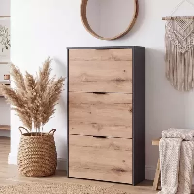 Móvel de madeira com três gavetas, espelho redondo pendurado, vaso de palha com plantas secas, tapete de fibras naturais e manta bege