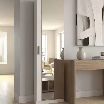 Roupeiro branco estreito com espelho numa divisão interior junto a secretária de madeira e vaso branco