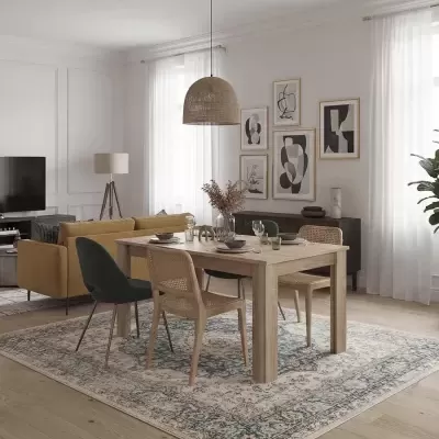 Sala de jantar e estar com mesa de madeira, cadeiras em vime e tecido, tapete padrão clássico, sofá amarelo e candeeiro em rattan