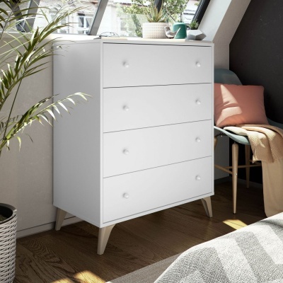 Cómoda branca de madeira com quatro gavetas e puxadores redondos perto de cadeira com almofada cor de salmão