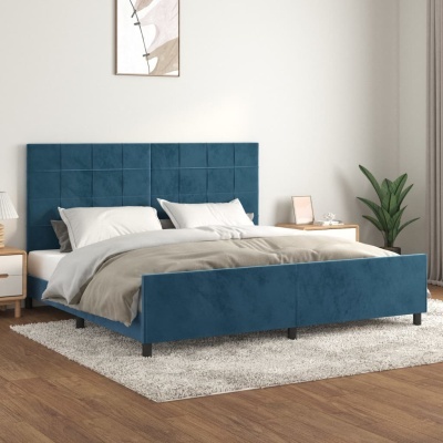 Cama de casal estofada azul com cabeceira acolchoada, roupa de cama branca e bege, mesas de cabeceira, tapete cinza e planta no quarto
