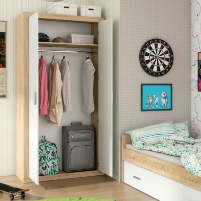 Guarda-roupa aberto com roupas e malas ao lado de cama em quarto decorado.