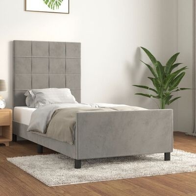 Cama individual estofada cinzenta com cabeceira quadrada, decorada com roupa de cama clara e planta ao lado